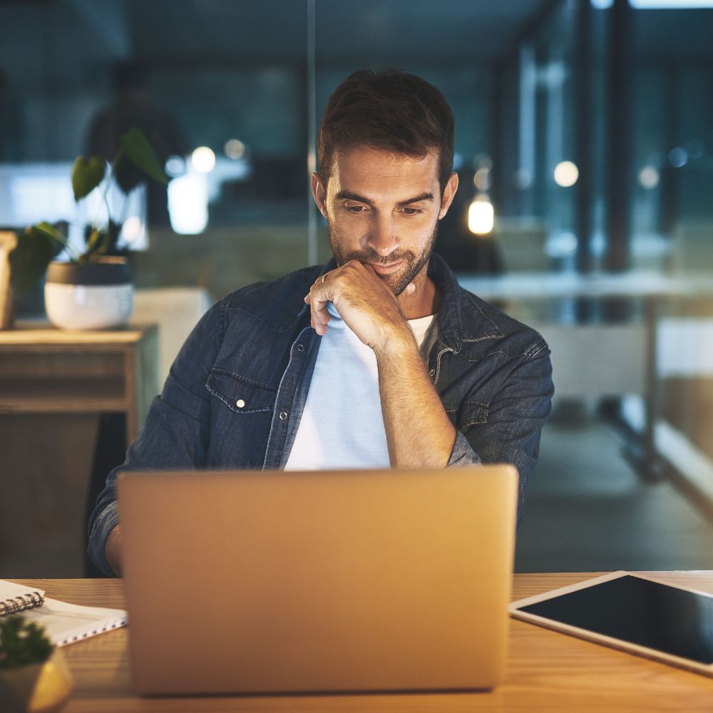 Man sitting at a desk in an office at night, using a laptop.